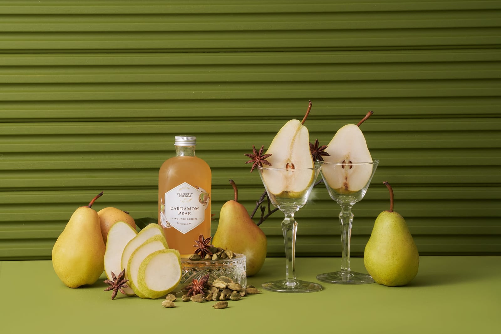 World Famous Cardamom Pear cordial styled with fresh pears, star anise and cardamom pods against an olive green wall